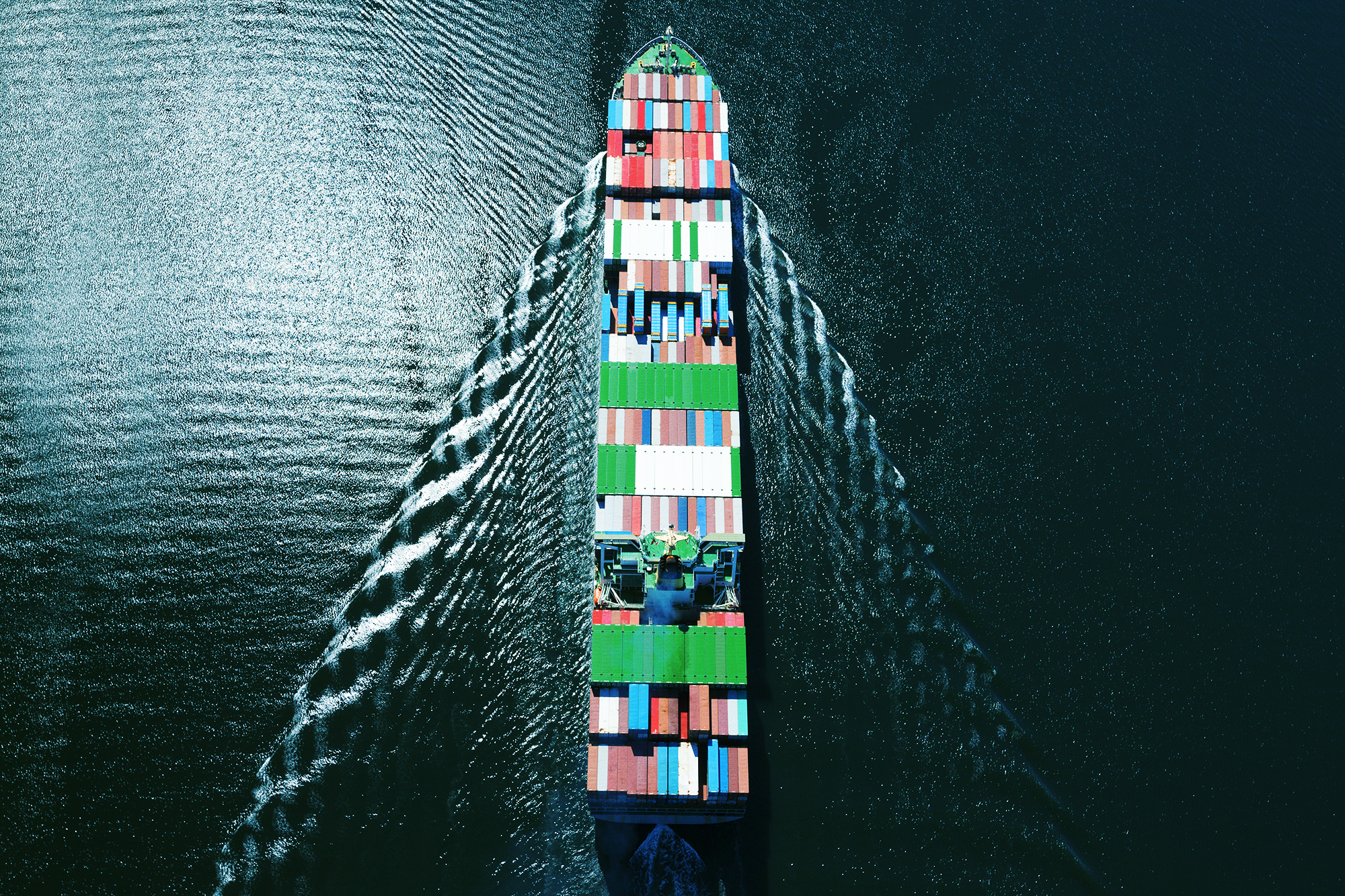 large cargo ship with containers moving through water from birds eye view